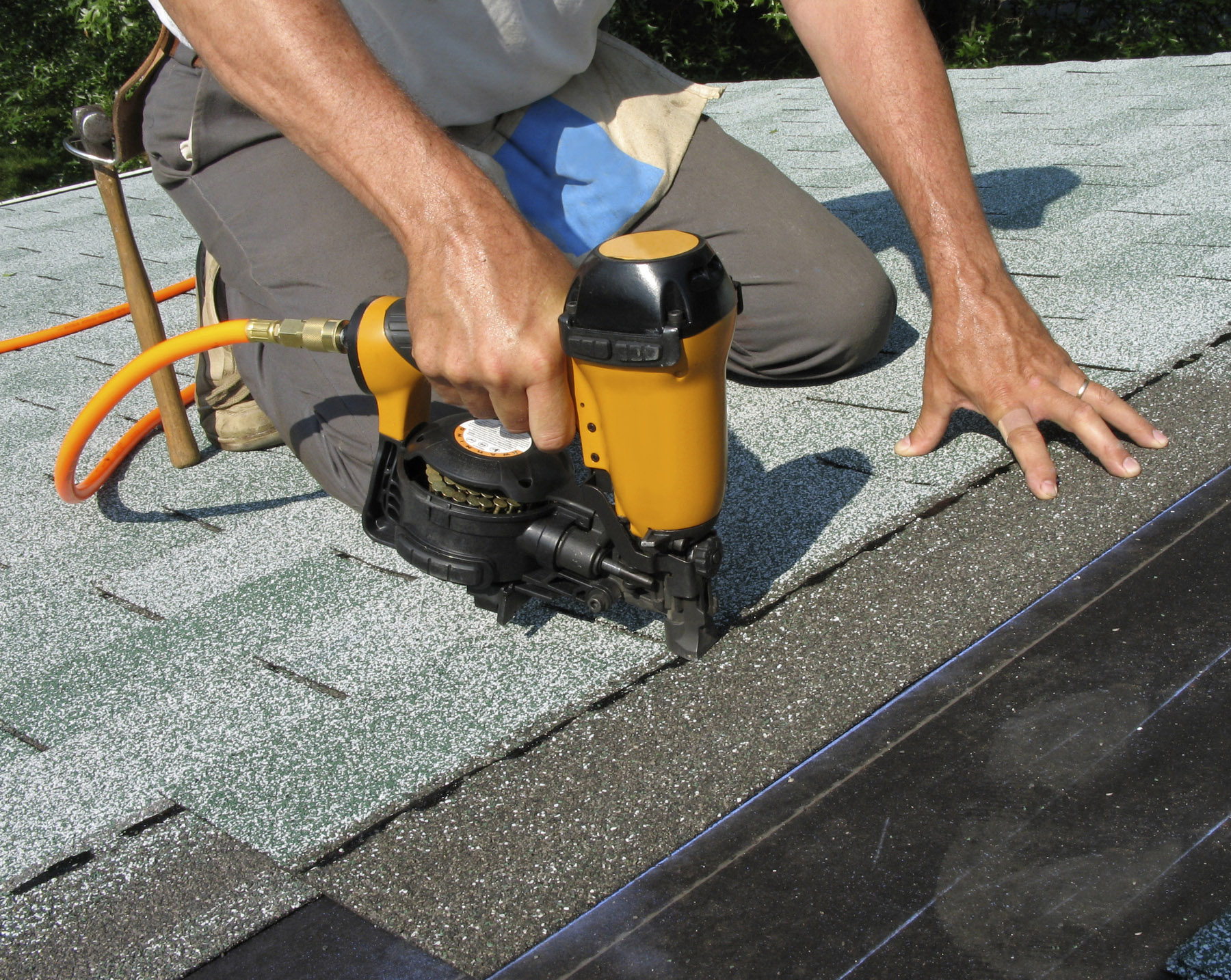 Roofing professional using a nail gun to nail down asphalt shingles.